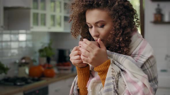 Worried woman wrapped in a blanket drinking hot tea