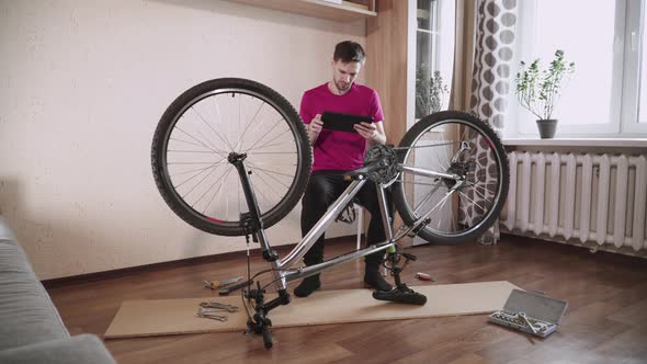 Amateur Cyclist Sits Near Broken Bike with Tablet Tries to Figure Out Problem