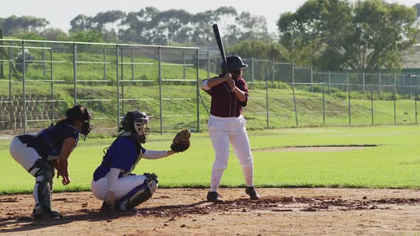 Diverse group of female baseball players playing on the field, hitter swinging for pitched ball