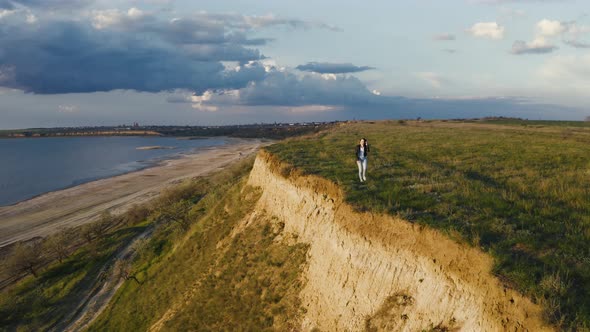 Tracking Aerial Shot of Young Woman Enjoying Sunset in Field Near the Cliff During Beatiful Sunset