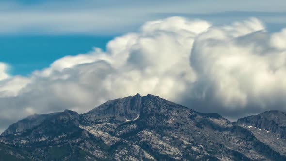 Time lapse of beautiful bellowing cumulus clouds forming above rugged mountain peaks while zooming o