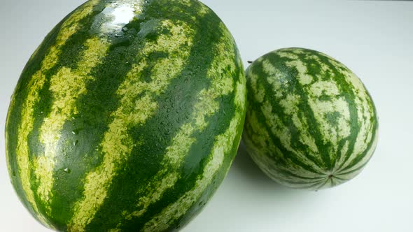 Two Watermelons On A White Surface Covered In Drops Of Water