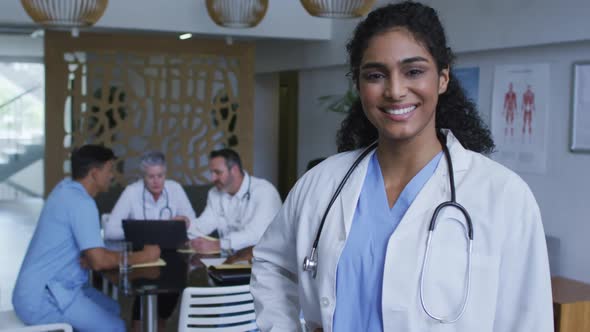 Portrait of asian female doctor smiling, with colleagues in discussion in background