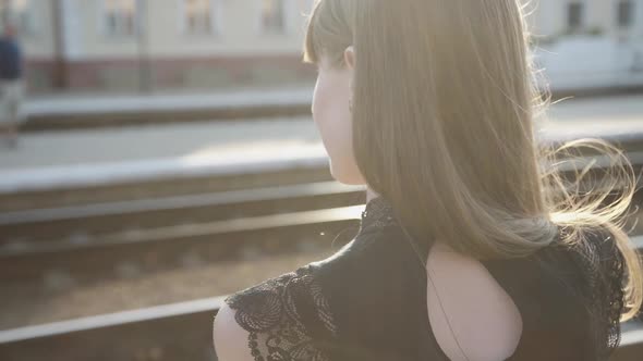 Portrait of Glamorous Girl with Blowing Hair Smiling on Sunset at Railway