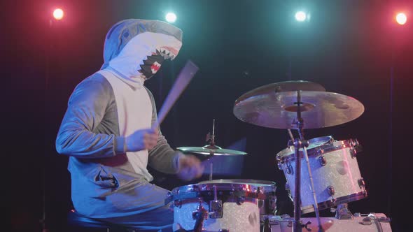 Side View of Musician in a Festive Shark Costume Plays Drums and Hits Percussion Cymbals