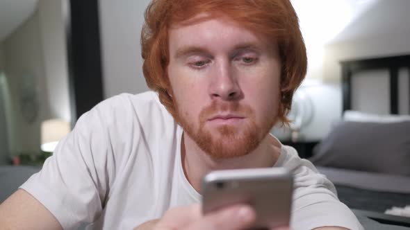 Casually Sitting Redhead Man Using Smartphone Browsing