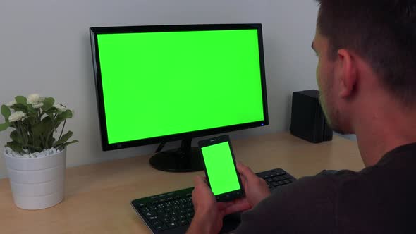 A Man Watches in Turns His Smartphone and a Computer Display, Both Green Screen