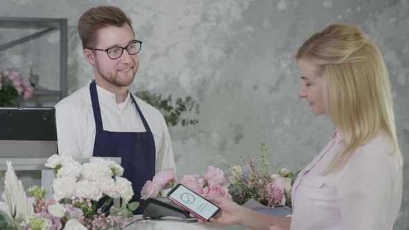 Contactless Payment, Male Seller in Flower Shop Sells Bouquet of Flowers To Female Buyer Pays