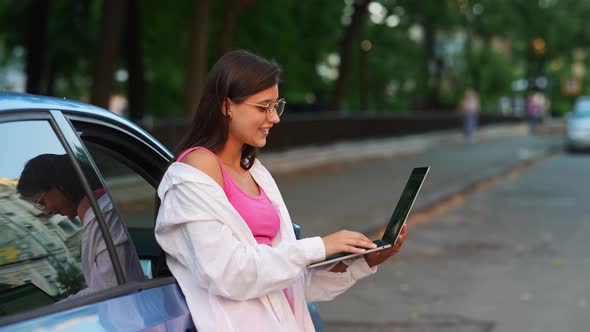 A Young Woman Uses a Laptop Near a Car