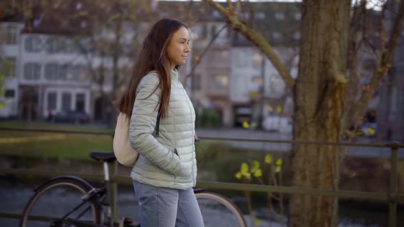 a Brunette with a White Backpack on Her Back Walks Along the City Embankment on a Sunny Day. a