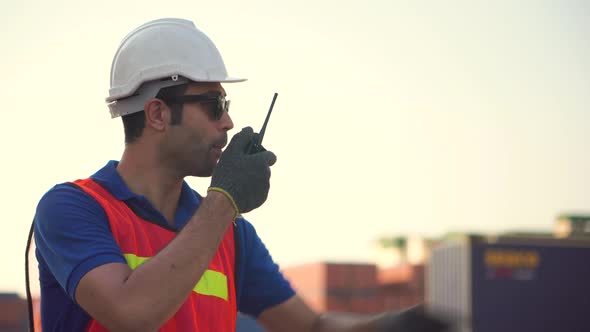 Foreman in hardhat and safety vest talks on two-way radio control loading containers box from cargo