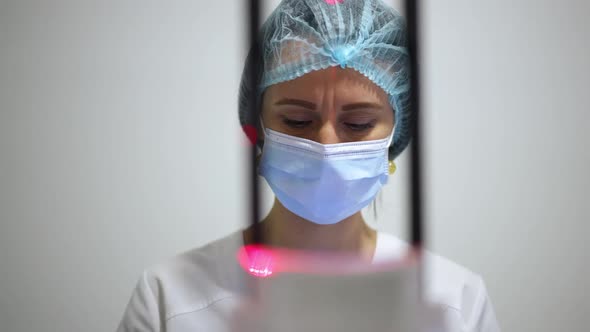 Concentrated Caucasian Woman in Face Mask Thinking Analyzing Xray Image of Teeth and Jaw Standing at