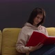 Attractive Longhaired Girl Sits at Home on Sofa and Smiling Reads Book - VideoHive Item for Sale