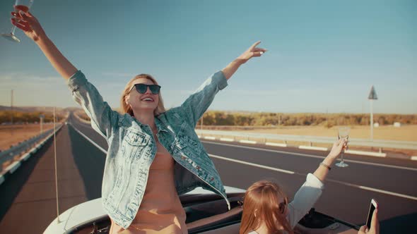 Two Happy Girls Ride in Convertible Enjoying Life with Their Hands Up
