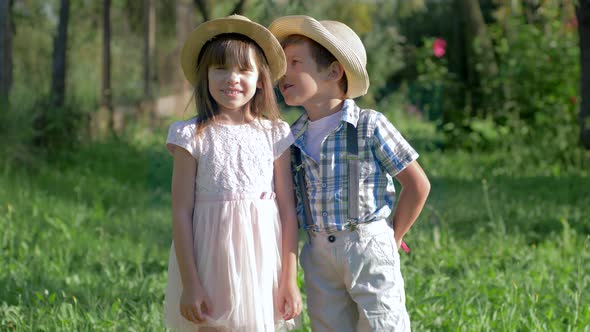 Childhood, Kid Whispers in Ear a Secret To a Cute Little Girl and Gives a Flower Outdoors at Summer