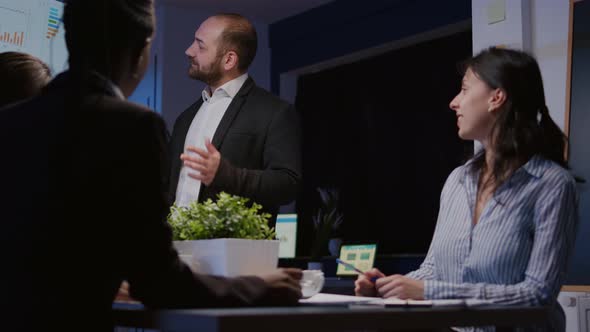 Overworked Businessman Presenting Management Statistics Using Presentation Monitor Late at Night