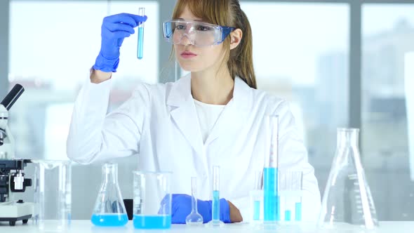 Female Research Scientist Looking at Blue Solution in Test Tube in Laboratory