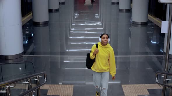 Young Girl Coming Up the Stairs in Modern Train Station Wearing Headphones