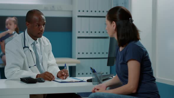 Male Doctor Having Conversation with Mother at Examination Appointment