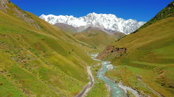 Aerial View of a River in a Mountain Valley Against the Backdrop of a Snowcapped Mountain Range