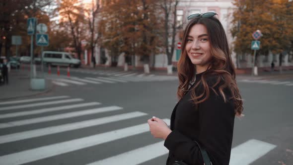 A Trendy Young Girl with Sunglasses on Her Head Stands Near a Pedestrian Crossing and Laughs