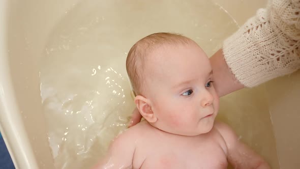 Closeup of Mother Supporting Baby Head While Washing in Bath