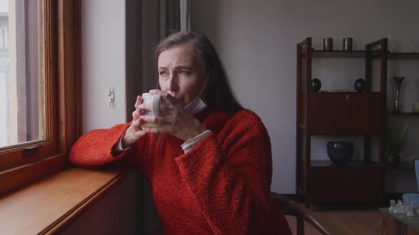 Woman drinking coffee while looking out of the window at home