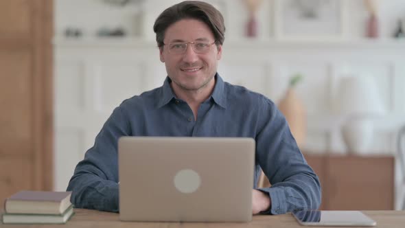 Young Man Smiling at Camera while using Laptop in Office