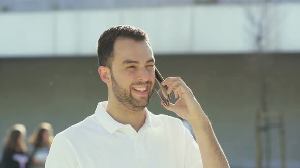 Young Man Having Pleasant Conversation Through Phone Outdoor