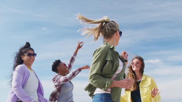 Happy group of diverse female friends having fun, dancing and smiling at the beach