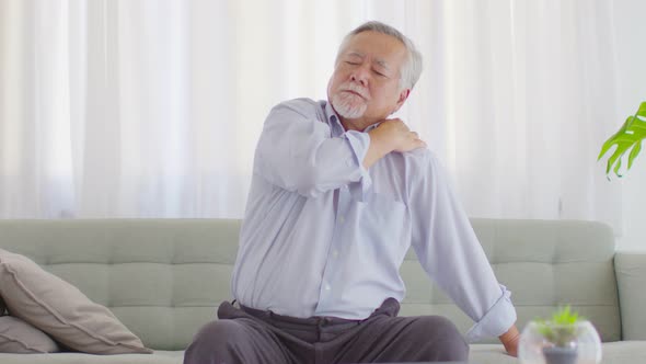 Asian Elderly senior man with white hairs shoulder pain and illness on sofa at home