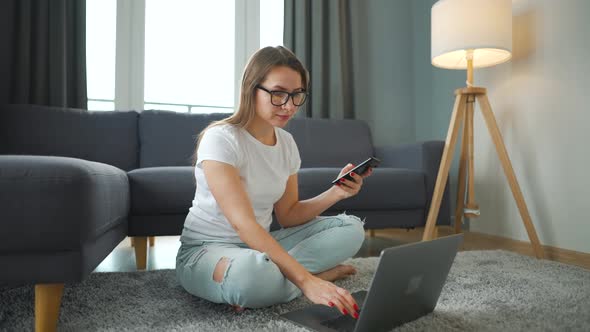 Casually Dressed Woman Sitting on Carpet with Laptop and Smartphone and Working in Cozy Room