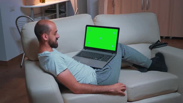 Tired Man Sitting on Sofa While Browsing Marketing Information Using Laptop Computer