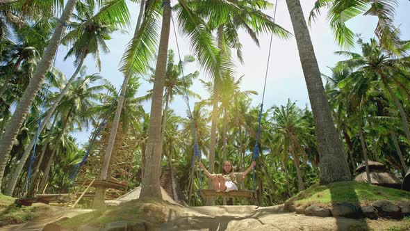 A Girl Swings on a Swing and Looks at the Sunset on a Tropical Seashore. Freedom, Rest, Vacation