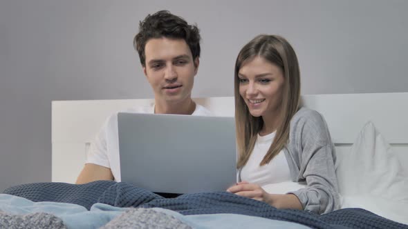 Happy Young Couple Using Laptop in Bed