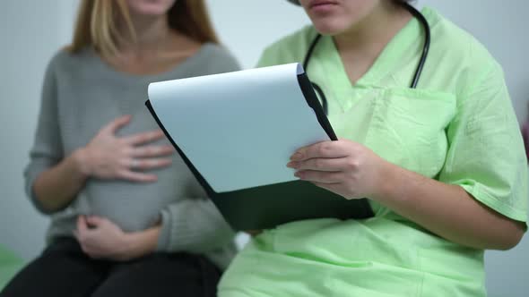Unrecognizable Obstetrician Filling in Medical History Sitting with Pregnant Patient on Examination