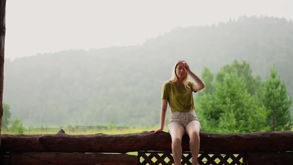 Attractive Lady Touches Hair Sitting on Log Against Mountain