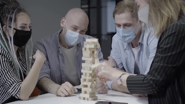 Relaxed Positive Group of Coworkers in Covid19 Face Masks Playing Jenga During Break in Office