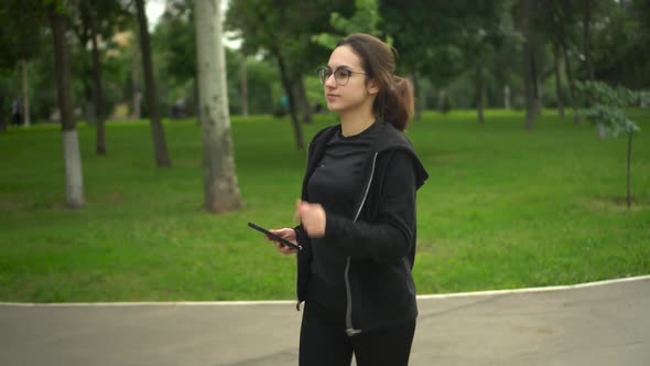 A Young Woman is Jogging with Her Phone in the Park