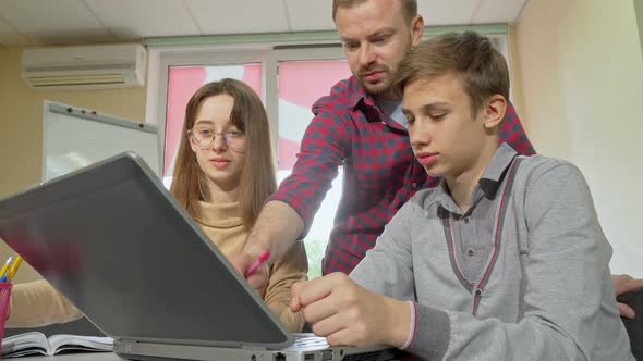 Mature Male Teacher Helping His Students with Assignment Using Laptop