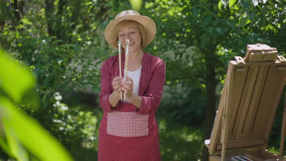 Portrait of Confident Happy Retiree Dancing with Painting Brushes Smiling Looking at Camera