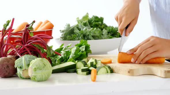 Mid-section of woman cutting vegetables on chopping board