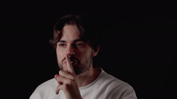 Trendy Young Man shushing into the camera, silence gesture, close, black background