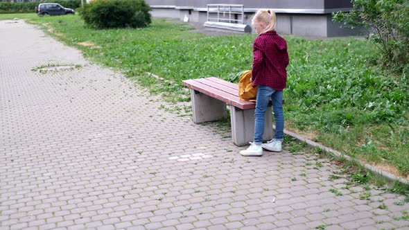 Back View Blonde Girl Puts Books Into Her Backpack on Street Near School