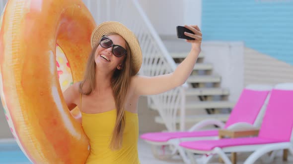 Young Attractive European Blonde Girl in Swimsuit and Hat Makes Selfie on Summer Pool Background