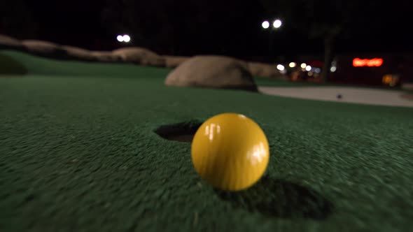 A yellow mini golf ball falls into the golf hole and bounces in the pocket on a course.