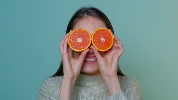 Female fooling around in front of camera with grapefruit.