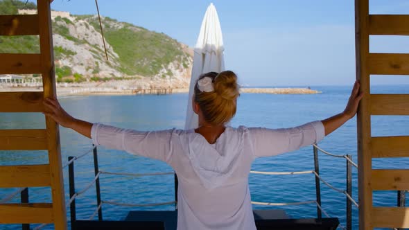 a Girl in a White Light Shirt and with a White Flower in Her Hair Looks at the Sea