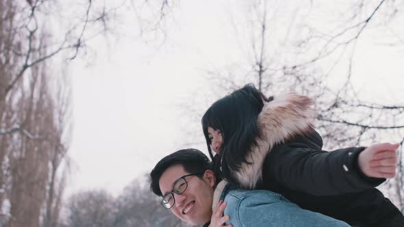 Young Man Giving Piggyback Ride To His Girlfriend and Spinning Her in the Park on Snowy Winter Day