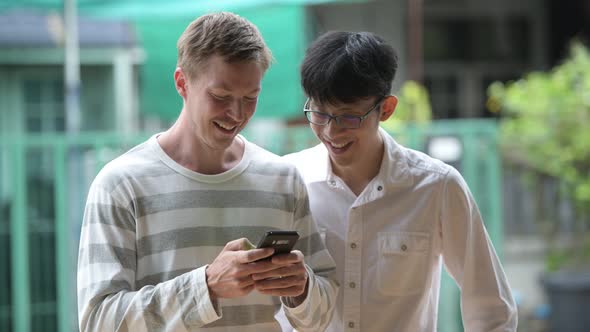 Two Happy Multi-ethnic Businessmen Smiling While Using Phone Together in the Streets Outdoors